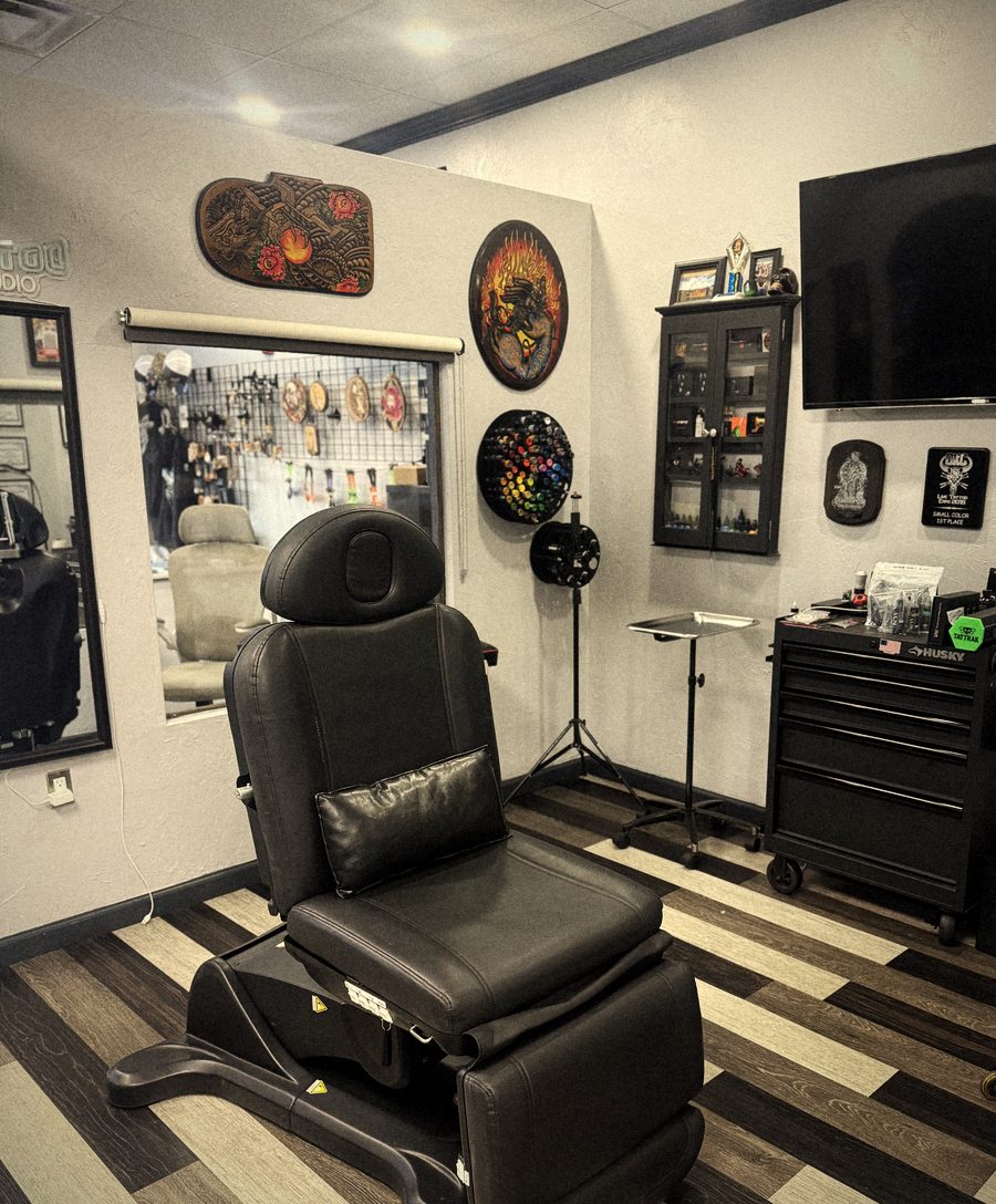 Black tattoo chair in an artist station with framed wall art, TV and rolling tool chest